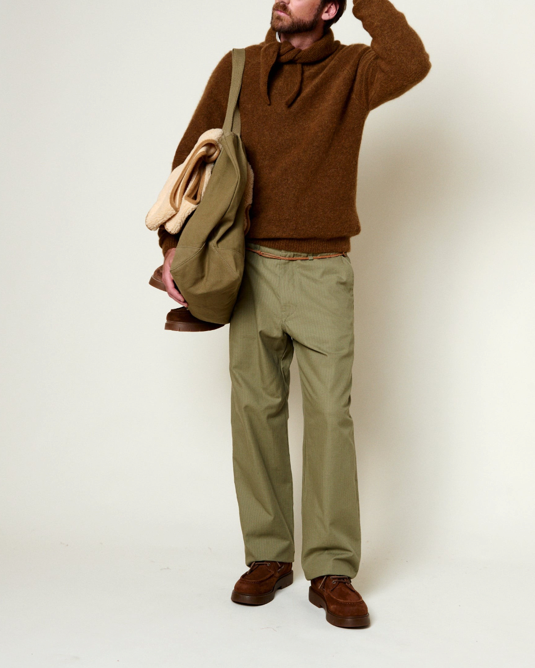 Homme portant un pull en alpaga marron Merci Paris avec un pantalon vert et un sac en toile sur fond clair