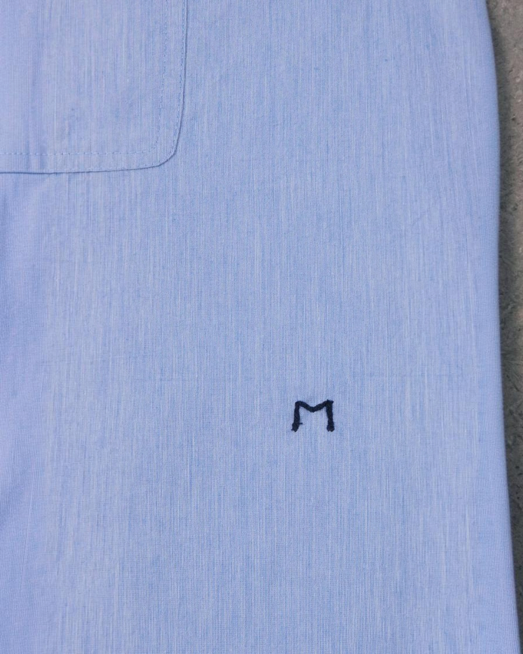 Gros plan sur la chemise Henriette Merci Paris en coton bleu clair avec broderie M signature