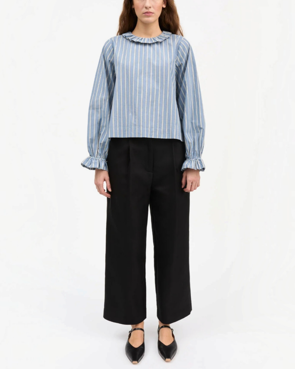 Modèle portant une blouse Skall Studio en coton biologique bleu à rayures, col rond volanté et manches bouffantes