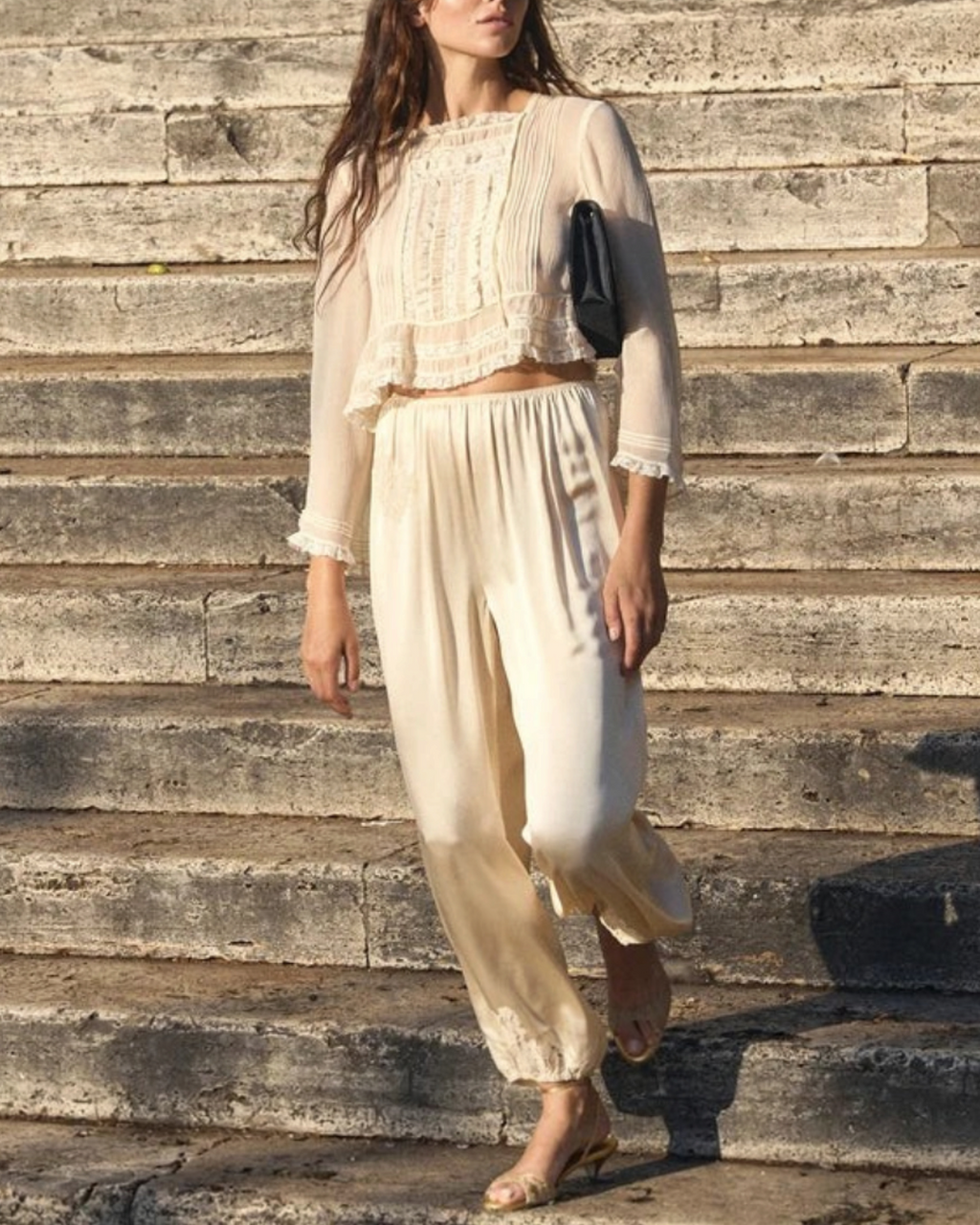 Modèle portant la blouse écrue Elodine de Merci Paris en soie avec dentelle et pantalon assorti sur des marches
