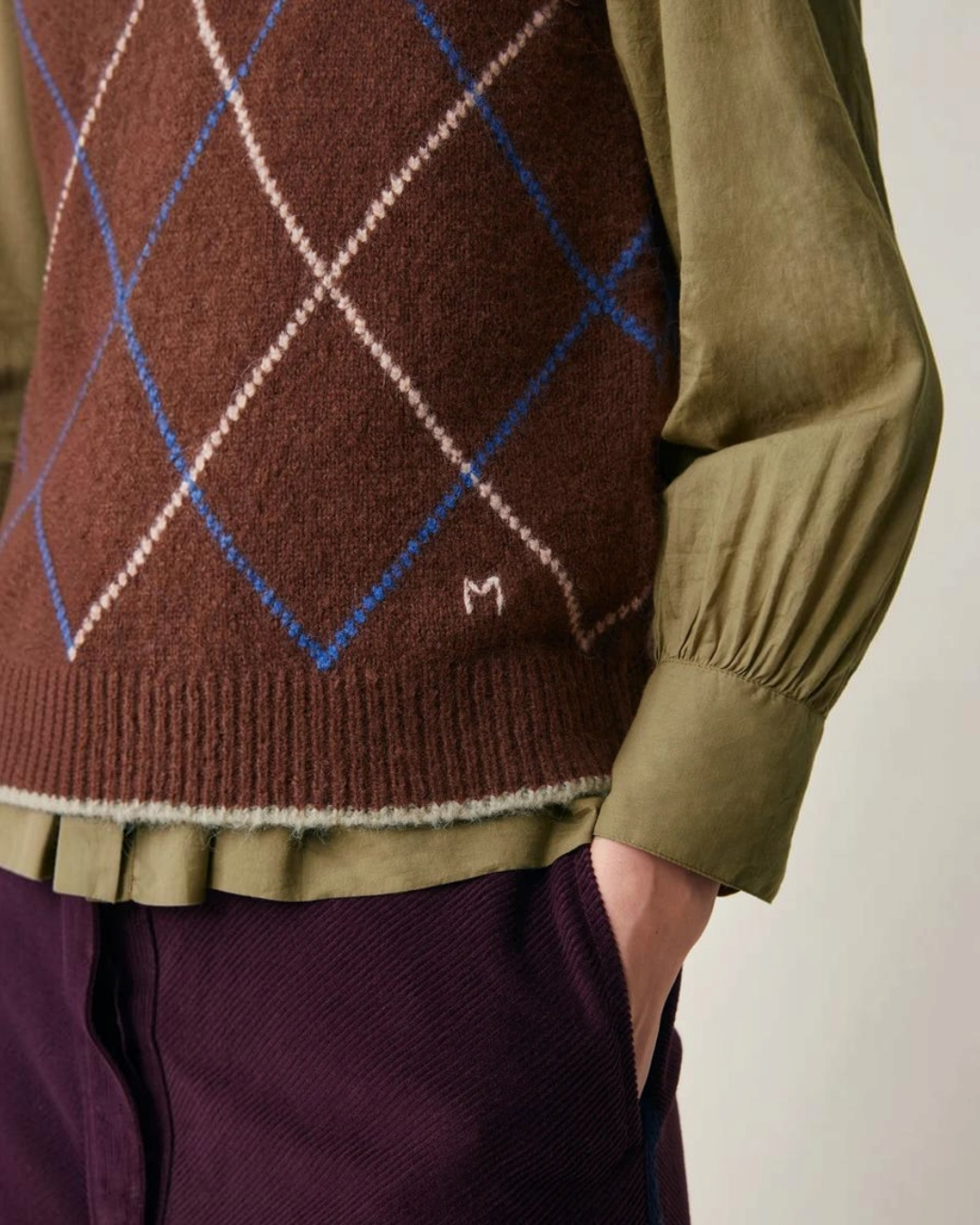 Pull sans manches Moismont Eddy en maille d'alpaga marron à motif losanges avec broderie M, porté sur une chemise