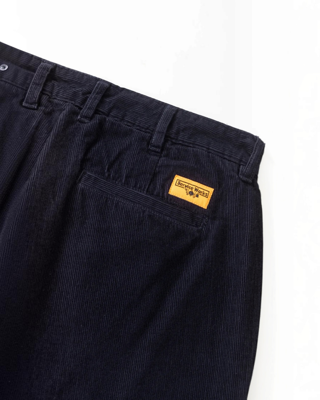 Pantalon en velours bleu marine Service Works avec poches et étiquette orange, disponible chez Merci Paris